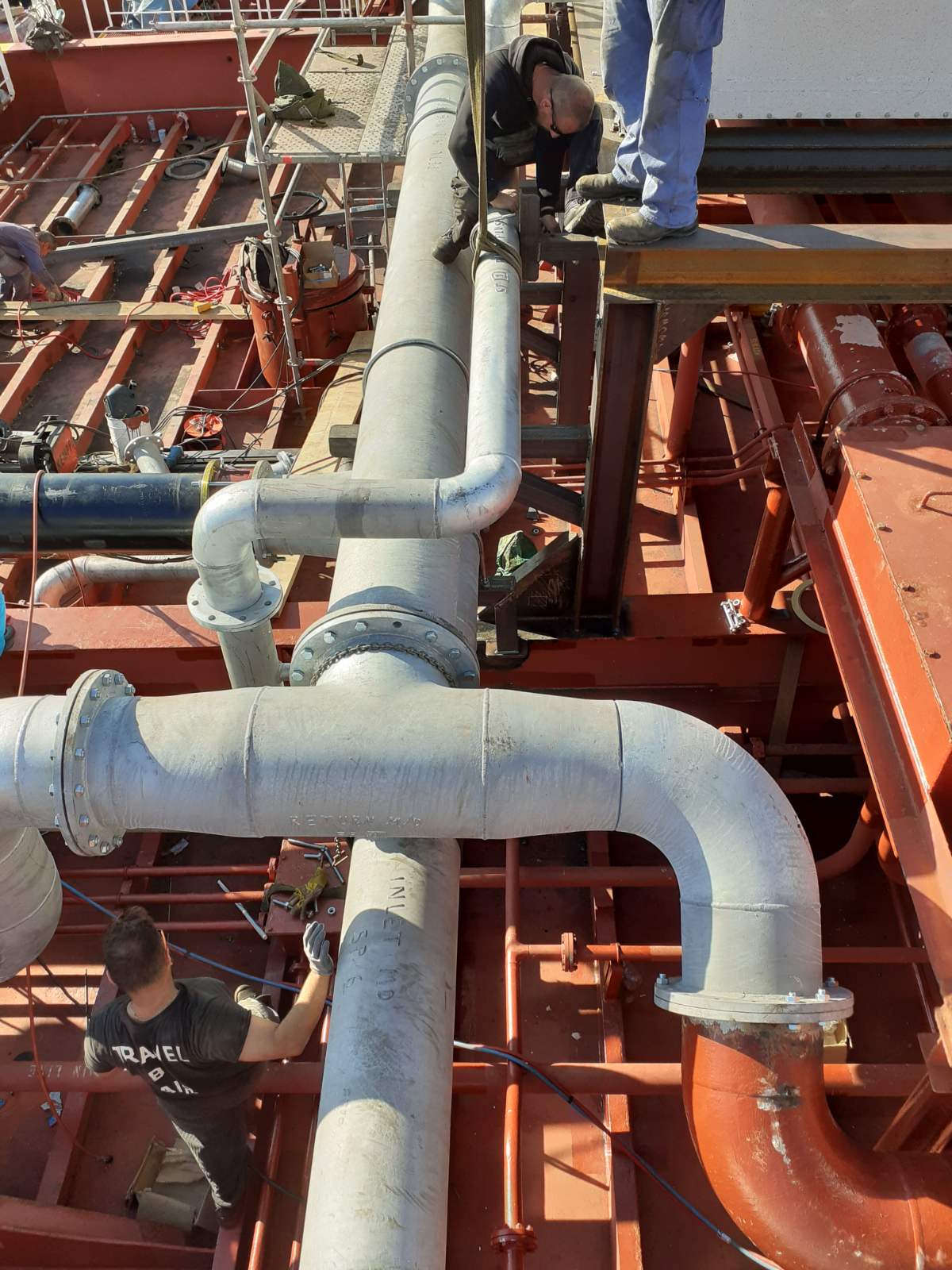 Technicians installing and aligning large-diameter marine piping on a vessel deck